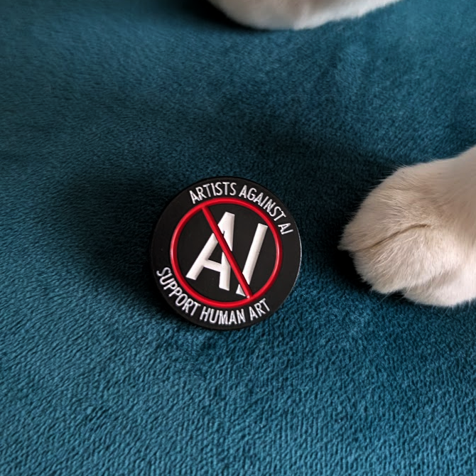 A round black enamel pin with a red prohibition symbol over white 'AI' lettering and the words 'ARTISTS AGAINST AI' and 'SUPPORT HUMAN AI', placed on a teal textured surface near a white cat's paw.