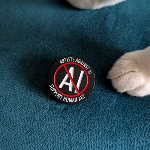 A round black enamel pin with a red prohibition symbol over white 'AI' lettering and the words 'ARTISTS AGAINST AI' and 'SUPPORT HUMAN AI', placed on a teal textured surface near a white cat's paw.