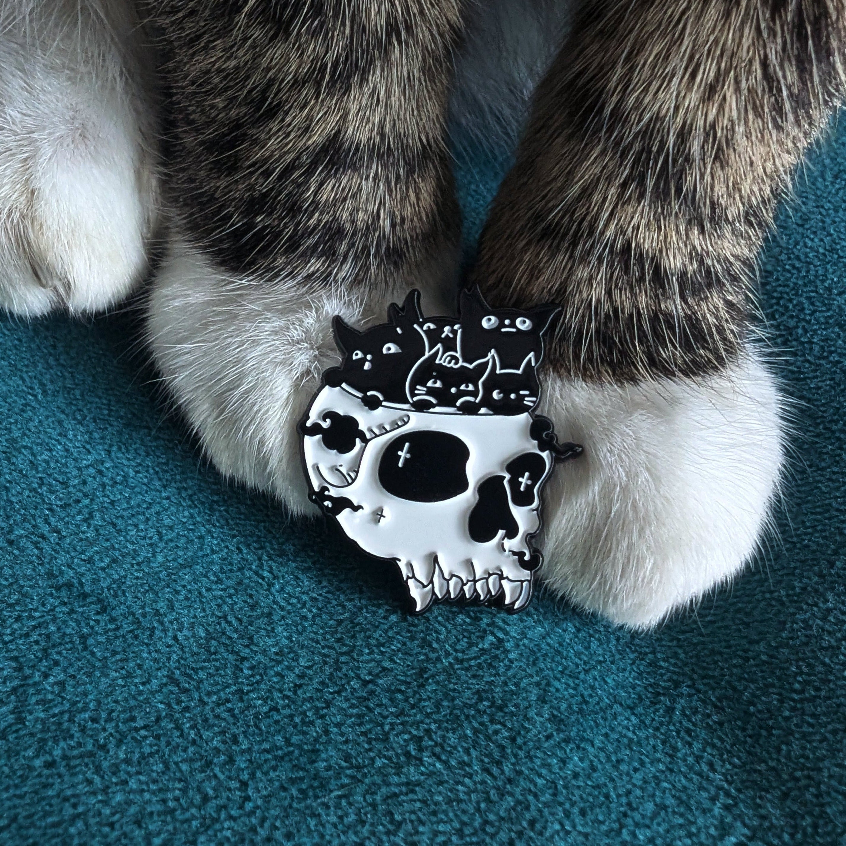 White skull-shaped pin with cat silhouettes.