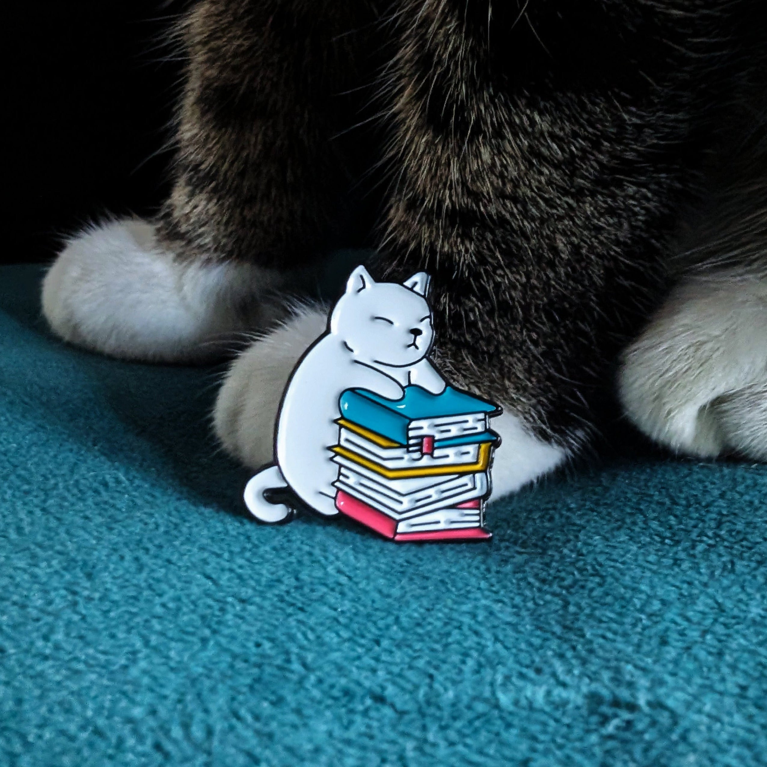 White cat sitting on stack of books enamel pin