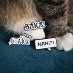 Pins with Japanese text next to a cat's paws. The pins read 'スグサ!' (Otaku!), 'スグン!' (Otaku!), and 'シグン!' (Nani?).