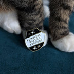 Cat's front paws standing on a dark teal textured surface, with a black pin text reading 'POINTLESS MEETING SURVIVOR'.