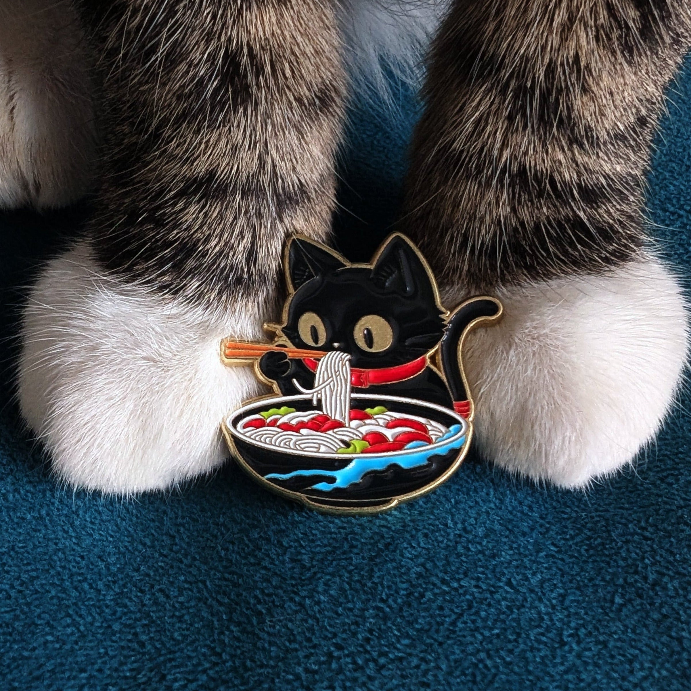 Enamel pin shaped like a black cat eating ramen with chopsticks.